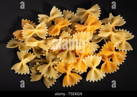 Colorato materie bow tie pasta su sfondo nero. Farfalle di pasta Foto Stock