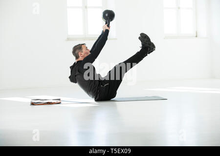 L uomo che sta facendo il suo regime fitness, bollitore facendo bell sit ups Foto Stock