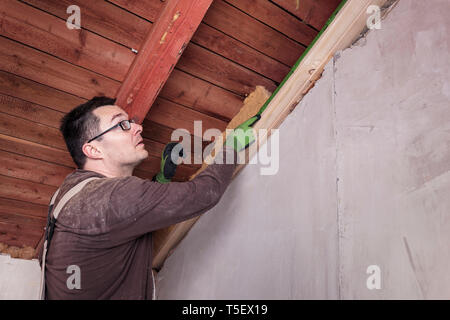 Isolamento del tetto, lavoratore il riempimento di falde del tetto in legno con isolamento in fibra Foto Stock