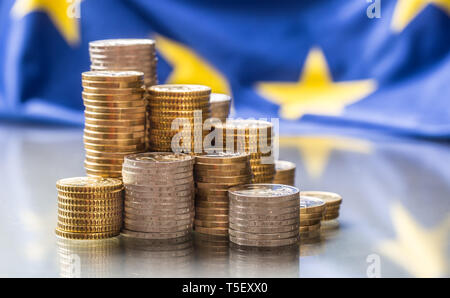 Torri con le monete in euro e la bandiera della Unione Europea in background. Foto Stock