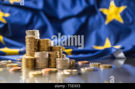 Torri con le monete in euro e la bandiera della Unione Europea in background. Foto Stock