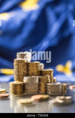 Torri con le monete in euro e la bandiera della Unione Europea in background. Foto Stock