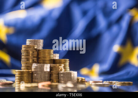 Torri con le monete in euro e la bandiera della Unione Europea in background. Foto Stock