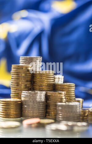 Torri con le monete in euro e la bandiera della Unione Europea in background. Foto Stock