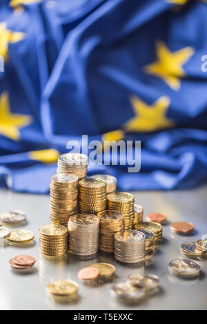 Torri con le monete in euro e la bandiera della Unione Europea in background. Foto Stock