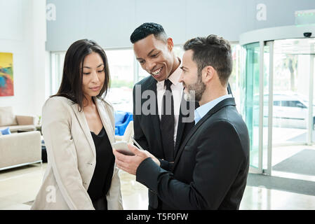 Imprenditore mostra smart phone ai suoi colleghi in hotel Foto Stock