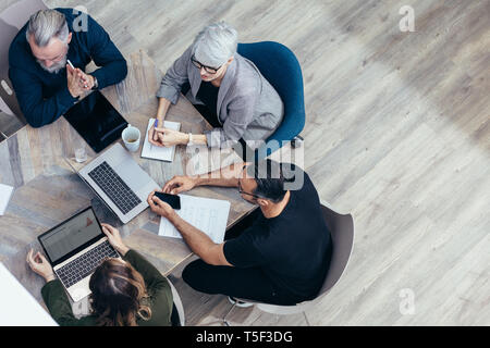 Il team di Business seduti attorno a un tavolo e di parlare su nuove idee. Angolo di alta vista del professionista aziendale avente una riunione in ufficio. Foto Stock