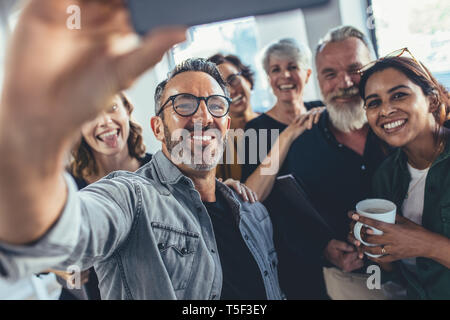 Gruppo di persone felici selfie prendendo in ufficio. Avvio di imprenditore in ufficio tenendo selfie con il suo team. Foto Stock