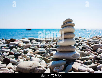Equilibrio di pietre sulla mano contro lo sfondo del mare. Il concetto di pace della mente, armonia, spiritualità Foto Stock
