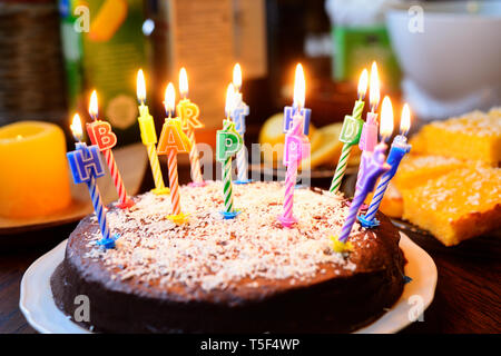 Una torta di compleanno con candele accese, iscrizione Buon compleanno Foto Stock