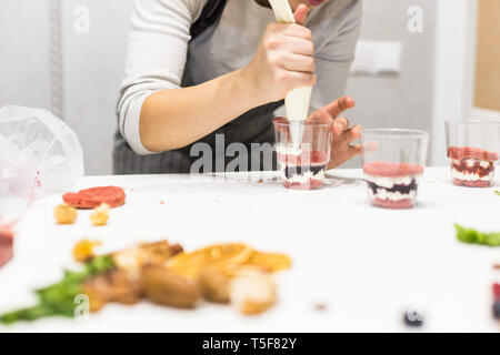 Un pasticcere prepara una inezia in tre tazze. I dessert sono sul tavolo bianco in cucina. Il concetto di dolci fatti in casa, la cottura di torte. Foto Stock