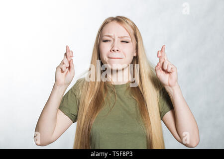 Giovane donna incrocia le dita, chiude gli occhi, anticipare l'udito la Buona Novella. Il linguaggio del corpo del concetto. Foto Stock