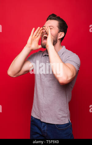 Ritratto di un allegro giovane uomo vestito con una camicia di denim in piedi isolato su sfondo rosso, urlando Foto Stock