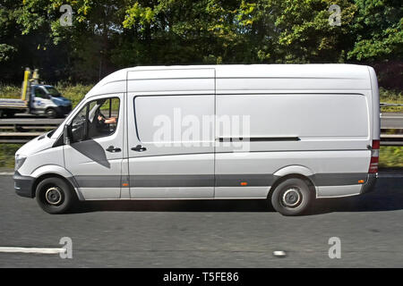 Vista laterale della luce bianca commerciale cargo van & driver guidando lungo la strada a doppia carreggiata stradale autostrada a tre corsie accanto a crash barriera England Regno Unito Foto Stock