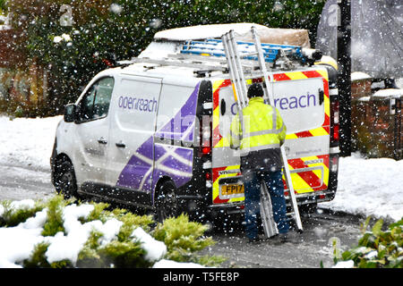 Inverno nevoso scena di strada di fiocchi di neve intorno a BT Openreach van & engineer alta vis jacket lavora con scaletta in caduta tempesta di neve England Regno Unito Foto Stock