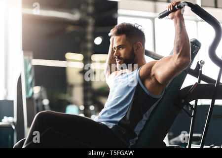 Giovane uomo che esercitano con apparecchiatura di allenamento in palestra, spazio vuoto Foto Stock