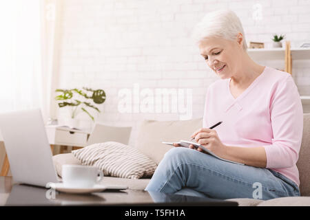 Senior donna scrivere pensieri e di lavoro sul computer portatile Foto Stock