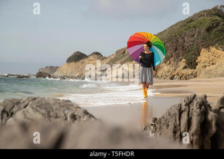 Donna con ombrello coloratissimo di camminare sulla spiaggia Foto Stock