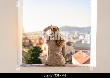 Vista posteriore di una giovane donna seduta su una parete Foto Stock