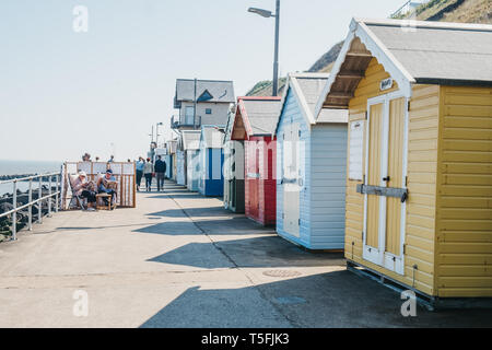 Sheringham, Regno Unito - 21 Aprile 2019: Gente seduta dalla pittoresca spiaggia di capanne sul mare a Sheringham in una giornata di sole. Sheringham è una località costiera inglese Foto Stock