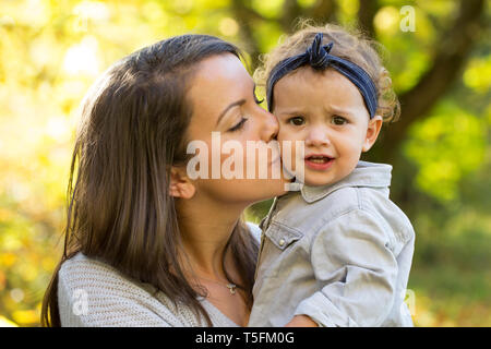 Madre baciare bambina all'aperto in autunno Foto Stock