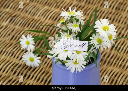 Get Well card con daisy fiori in vaso blu sulla superficie di vimini Foto Stock