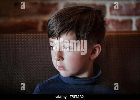 Razza mista Asian Caucasian boy con le braccia incrociate indossando blue turtleneck shirt nella parte anteriore del rosso parete di mattoni Foto Stock