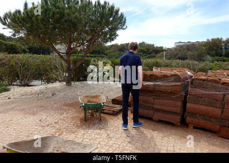 Ragazzo di unwrapping nuovi rotoli di manto erboso dal pallet Foto Stock