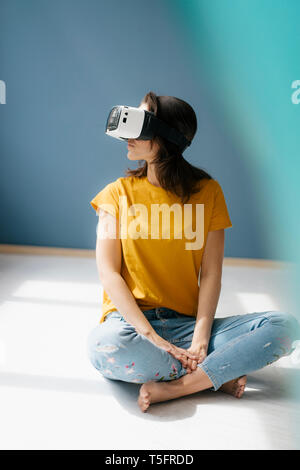 Donna seduta con le gambe incrociate sul pavimento, indossando occhiali VR Foto Stock