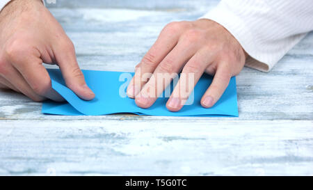 Chiudere fino a mani blu di piegatura del foglio di carta. Foto Stock