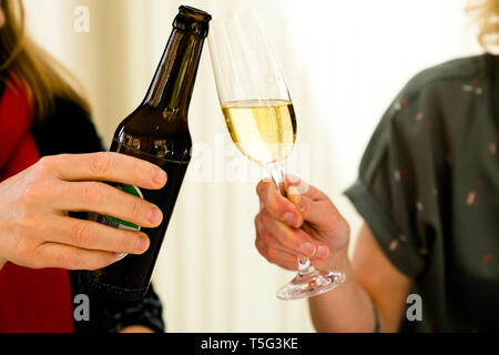 Vista in dettaglio di due donne che fanno un brindisi con una bottiglia di birra e un bicchiere di champagne Foto Stock