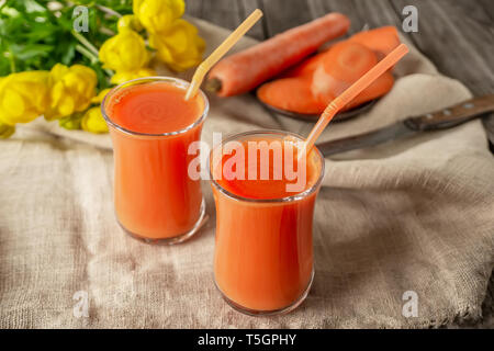 Freschi Fatti in casa succo di carota in due tazze di vetro. Con la carota e fiori bianchi. Foto Stock