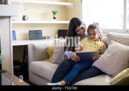 Felice madre e figlia seduti sul divano di casa utilizzando tablet Foto Stock