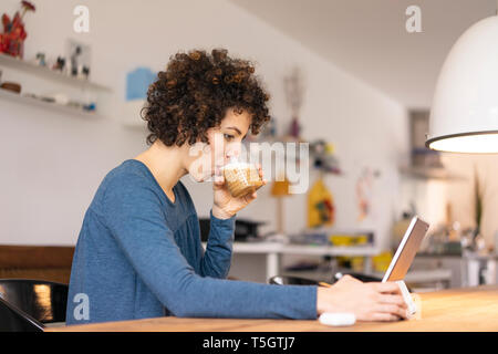 Giovane donna seduta a tavola, utilizzando digitale compressa, bere caffè Foto Stock