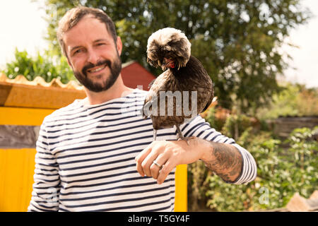 Ritratto di uomo sorridente con il polacco pollo a chickenhouse in giardino Foto Stock