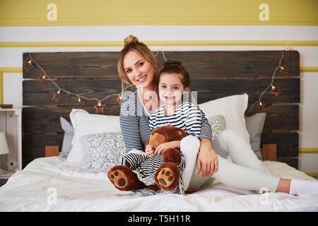 Madre e daighter seduta sul letto, ragazza honding orsacchiotto Foto Stock