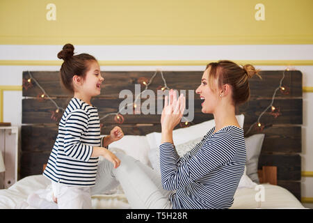 Madre e figlia divertirsi insieme, giocando, seduta sul letto Foto Stock