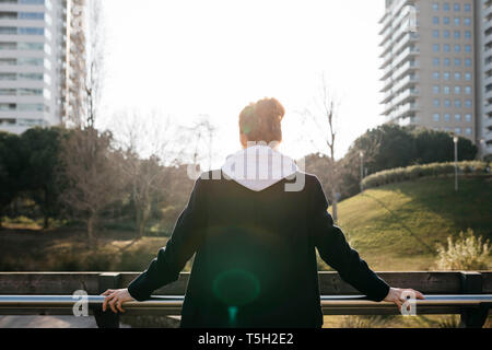 Vista posteriore del giovane donna appoggiata contro una recinzione in città Foto Stock