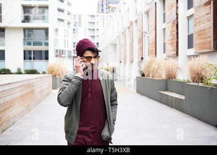 Ritratto di bello uomo barbuto in viola hat e vestiti in mirroring di occhiali da sole di effettuazione della chiamata tramite il telefono cellulare Foto Stock