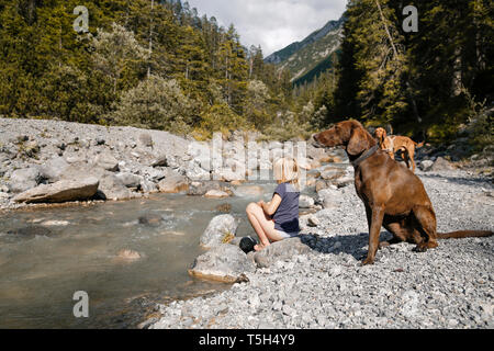 Austria, Tirolo, ragazza con due cani di un ruscello di montagna Foto Stock