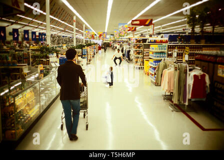 Vista posteriore di una donna spingendo un carrello di shopping all'interno di un supermercato. Foto Stock