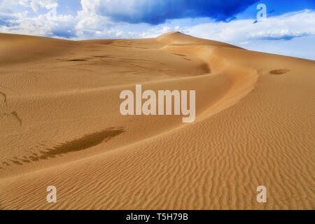 Esanime interminabili dune di sabbia sotto il cielo blu con stormy cloud computing con la luce del sole e la forte modello sulla superficie del terreno da erosione di vento. Foto Stock