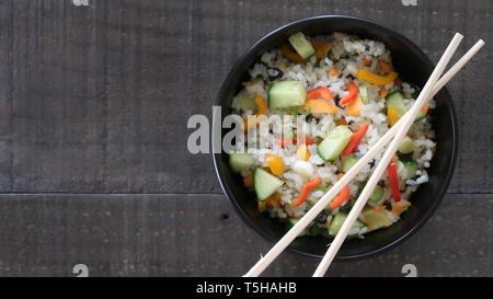 Insalata di sushi in una ciotola con bacchette su una tavola in legno rustico Foto Stock