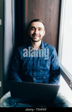L'uomo nelle cuffie lavorando su laptop e seduto sul davanzale Foto Stock