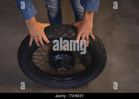 Moto meccanico di contenimento del pneumatico mentre in piedi in garage Foto Stock