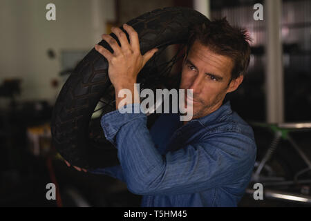 Moto meccanico di contenimento del pneumatico mentre in piedi in garage Foto Stock