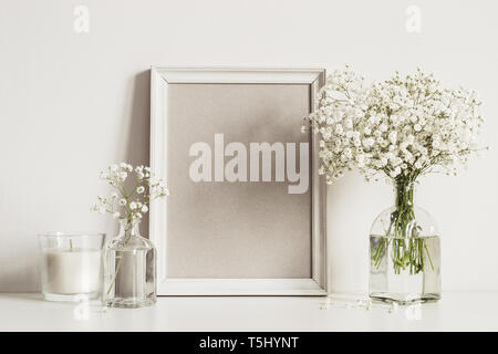 Mockup composizione con photo frame, fiori di colore bianco e la candela. Copia spazio per opere d'arte. Foto Stock