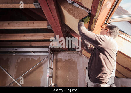 Isolamento del tetto, lavoratore il riempimento di falde del tetto in legno con isolamento in fibra Foto Stock