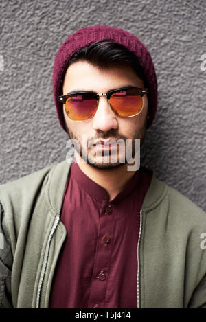 Ritratto di elegante uomo barbuto in camicia cachi, viola camicia e cappello e occhiali da sole su sfondo a trama Foto Stock