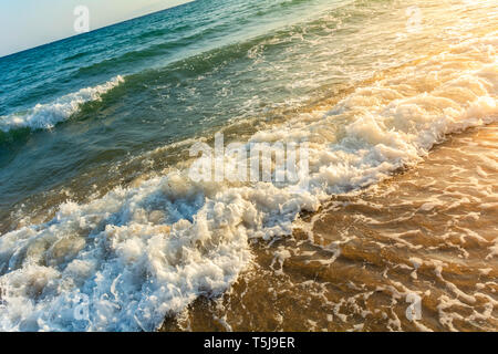 Diagonale inclinata colpo di mare oceano onde frantumazione su Riva - Sea Wave frantumazione della riva sotto il sole dorato - la luce del sole sulle onde dell'oceano inclinazione a sinistra Foto Stock